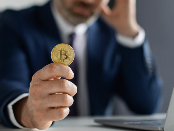 Crypto. Businessman Holding Bitcoin While Sitting At Desk With Laptop In Office.