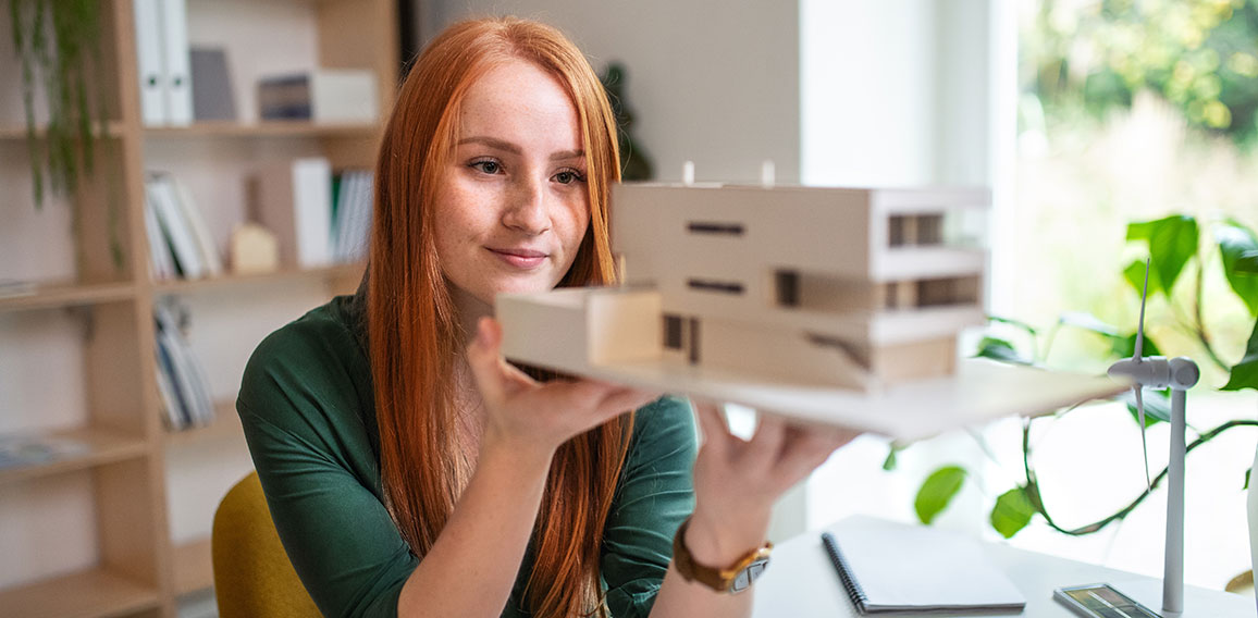 Architect with model of a house sitting at the desk indoors in office, working.