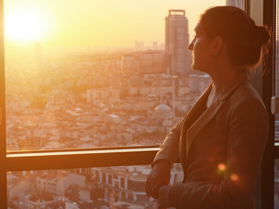 Young businesswoman in office standing near the window with panoramic city view.