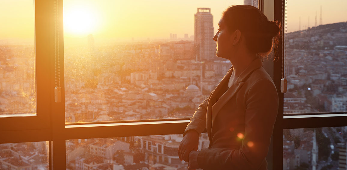 Young businesswoman in office standing near the window with panoramic city view.