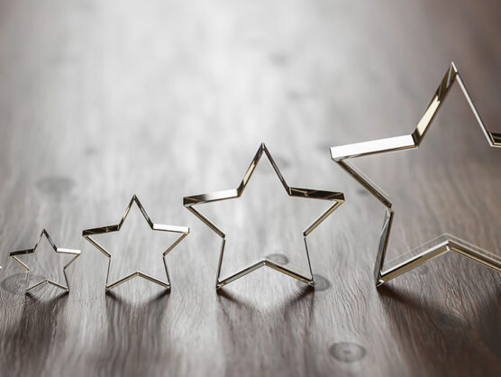 Rating - five transparent acrylic glas stars in different sizes arranged by size on a wooden table. Selective focus and copy space.