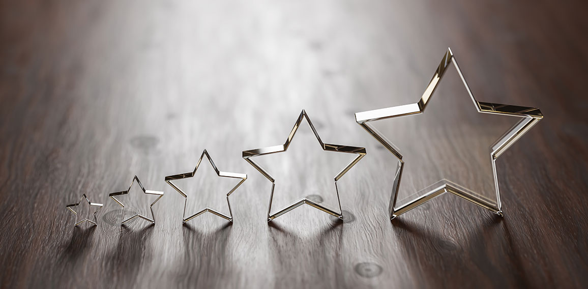 Rating - five transparent acrylic glas stars in different sizes arranged by size on a wooden table. Selective focus and copy space.