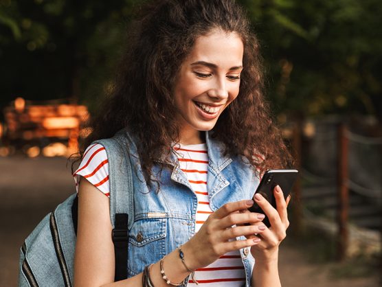 Lächelnde, junge Frau mit Rucksack und Smartphone in der Hand