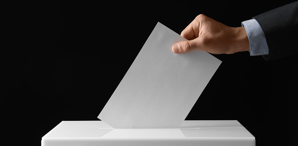 Hand steckt Wahlschein in Wahlurne