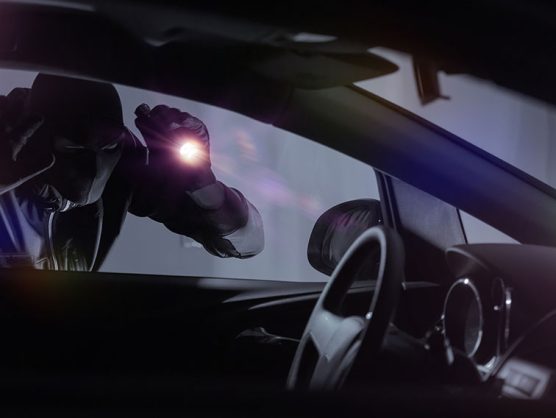 Autodieb leuchtet mit Taschenlampe in parkendes Auto