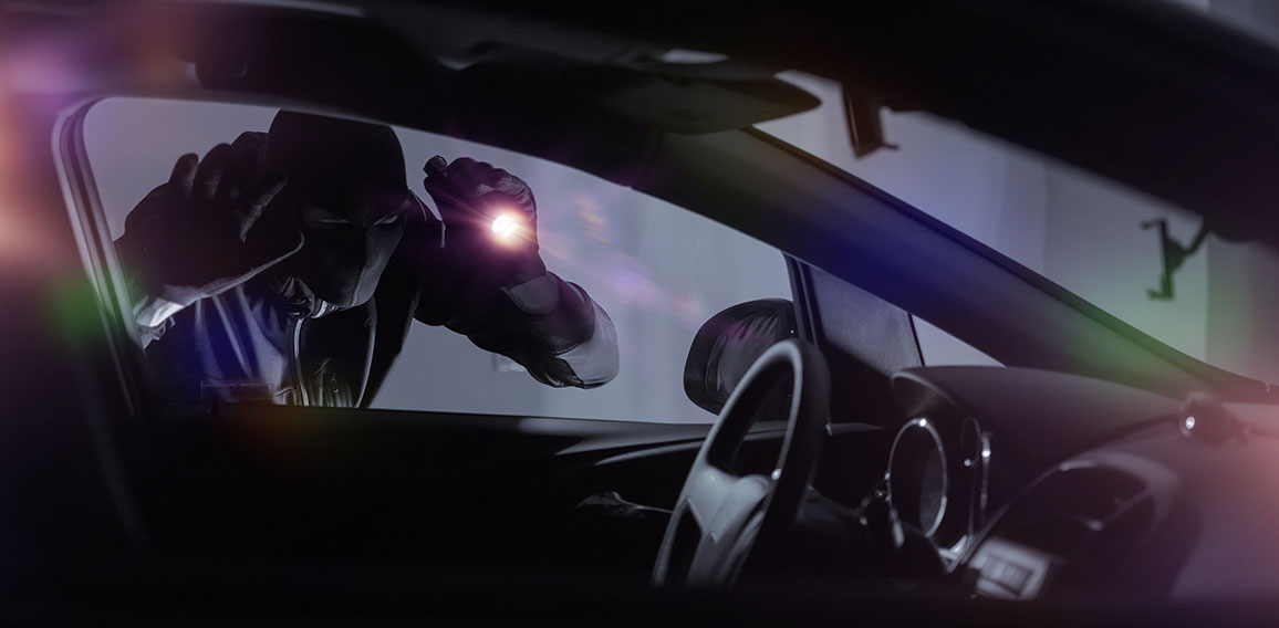 Autodieb leuchtet mit Taschenlampe in parkendes Auto