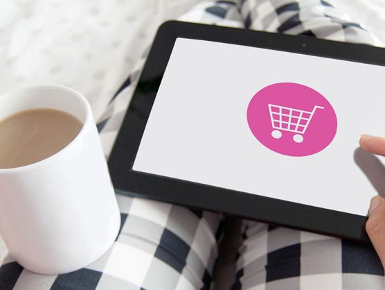 Frau mit Kaffee und Tablet auf dem Schoß shoppt online