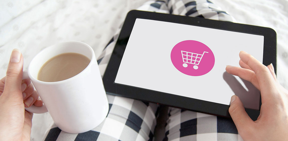 Frau mit Kaffee und Tablet auf dem Schoß shoppt online