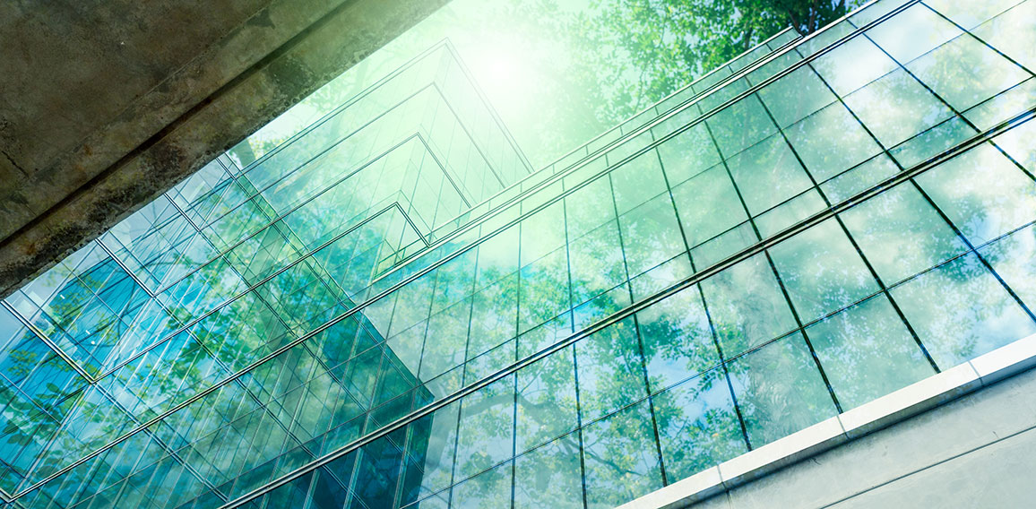 Bäume spiegeln sich in Glasfassade von Bürogebäude