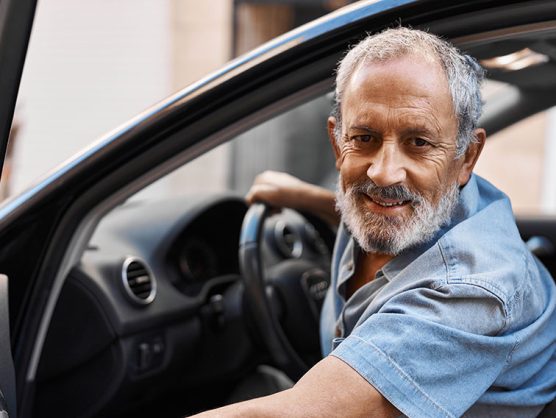 Älterer Fahrer steigt lächelnd in Auto