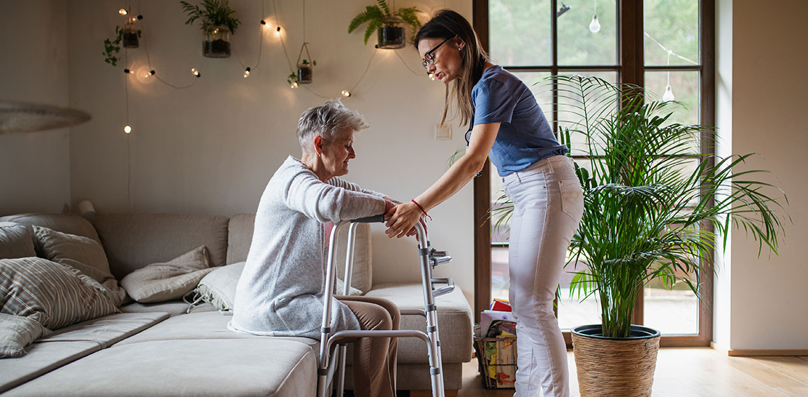 Pflegekraft hilft Seniorin aufzustehen