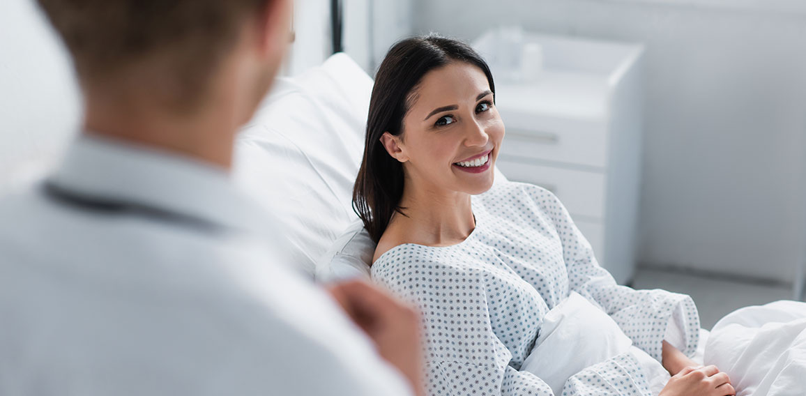 Patientin in Krankenbett lächelt Arzt an