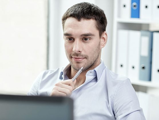 Mann in Büro blickt lächelnd auf Computer-Bildschirm