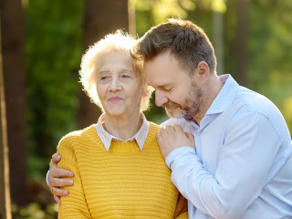 Loving adult son tenderly embracing his joyful elderly mother during walking at summer park. Mother's day holiday.