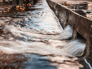 Stormy water on the sidewalk in a strong stream through curbs