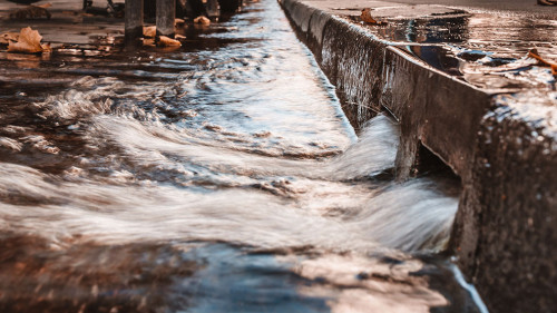 Stormy water on the sidewalk in a strong stream through curbs