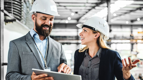 A portrait of an industrial man and woman engineer with tablet in a factory, working.