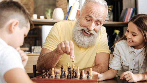 Little girl watching her brother and grandfather play chess