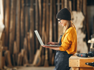young female carpenter looks drawings on a laptop during a break in work in workshop