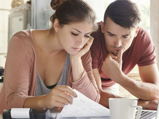 Worried young Caucasian married couple reading important notification from bank while managing domestic finances and calculating their expenses at kitchen table, using laptop computer and calculator