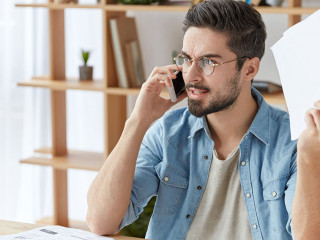 Shot of serious angry male enterpreneur tries to prove his rightness, has qaurrel with boss over smart phone, holds papers, solve company`s problems together. Annoyed boss shouts at colleague