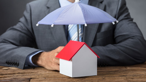 Businessman Protecting House Model With Umbrella