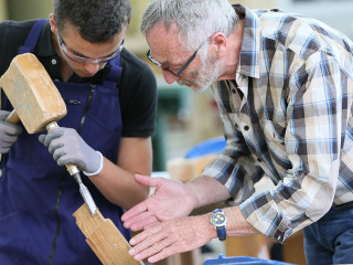 Young apprentice with teacher working on piece of wood