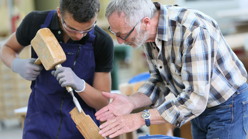 Young apprentice with teacher working on piece of wood