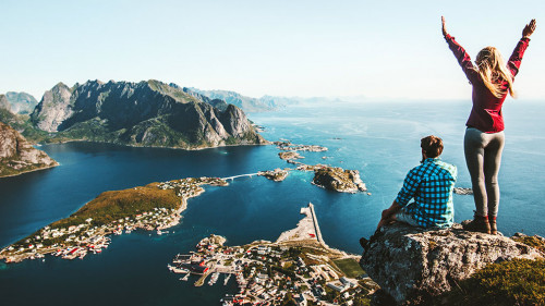 Couple family traveling together on cliff edge in Norway man and woman lifestyle concept summer vacations outdoor aerial view Lofoten islands Reinebringen mountain top