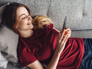 Girl using phone while lying on sofa at home