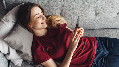 Girl using phone while lying on sofa at home