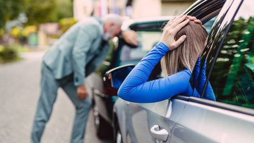 Senior man and young woman arguing after car crash.