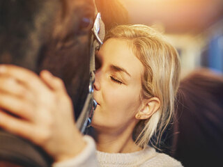 Young woman hugging her horse in stables before a ride
