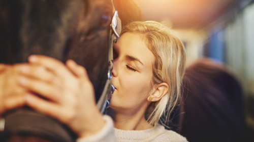 Young woman hugging her horse in stables before a ride