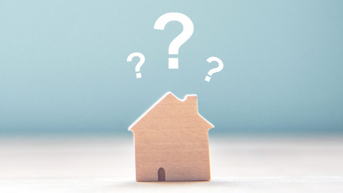 Wood House Model with question marks over the wooden desk and fr