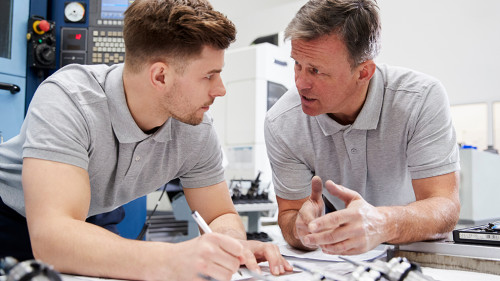 Engineer Showing Apprentice How To Measure CAD Drawings