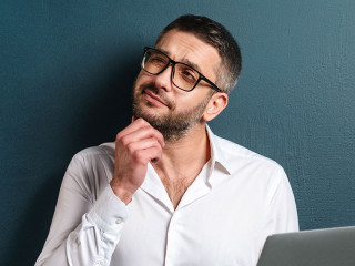 Thoughtful man wearing glasses using laptop computer.