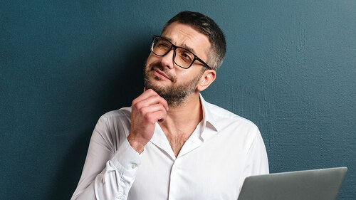 Thoughtful man wearing glasses using laptop computer.