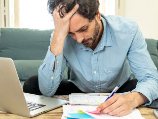angry man paying bills as home with laptop and calculator