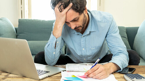 angry man paying bills as home with laptop and calculator