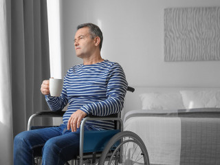 Mature man in wheelchair drinking coffee near window indoors
