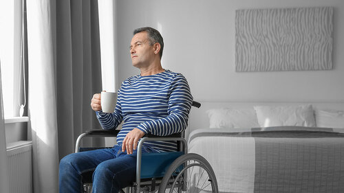Mature man in wheelchair drinking coffee near window indoors