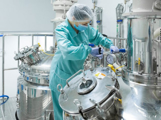 Pharmaceutical factory woman worker in protective clothing operating production line in sterile environment
