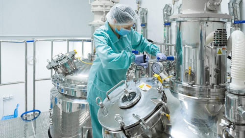 Pharmaceutical factory woman worker in protective clothing operating production line in sterile environment