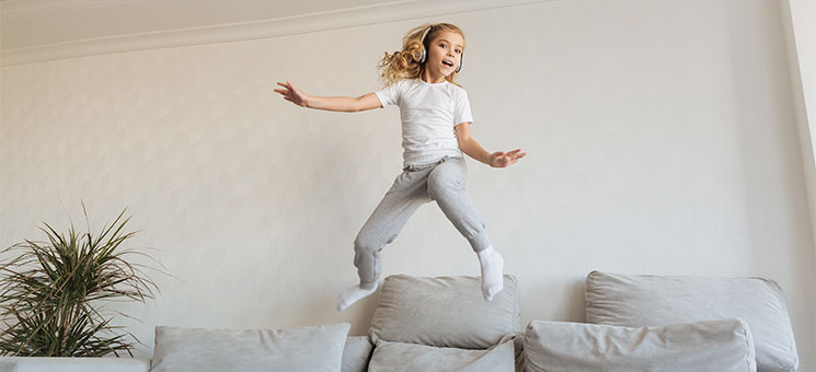 Maedchen-springt-auf-Sofa-189745337-AS-LIGHTFIELD-STUDIOS
