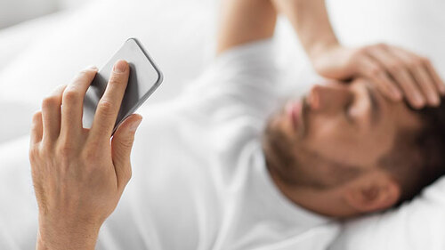 Mann-Bett-Smartphone-Kopfschmerzen-256398955-AS-Syda-Productions