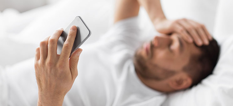 Mann-Bett-Smartphone-Kopfschmerzen-256398955-AS-Syda-Productions