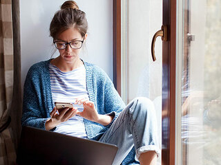 Frau-Fenster-Handy-Laptop-329840435-AS-Marina-Andrejchenko