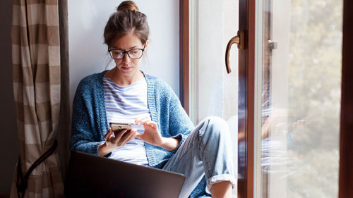 Frau-Fenster-Handy-Laptop-329840435-AS-Marina-Andrejchenko