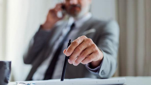 A midsection of businessman with smartphone sitting at the table, making a phone call.
